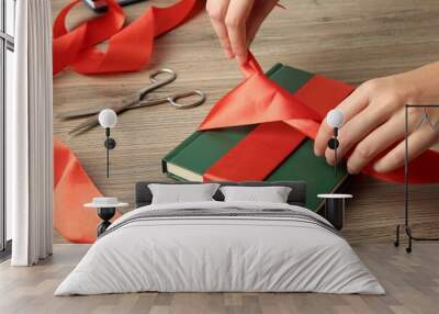 Woman tying ribbon on book at wooden table, closeup Wall mural