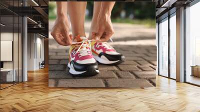 Woman tying shoelace of sneaker outdoors, closeup. Space for text Wall mural