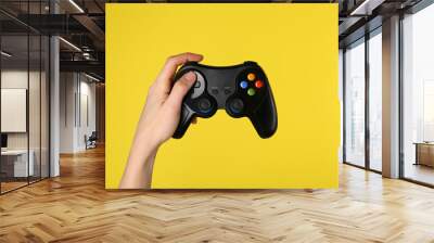 Woman using game controller on yellow background, closeup Wall mural