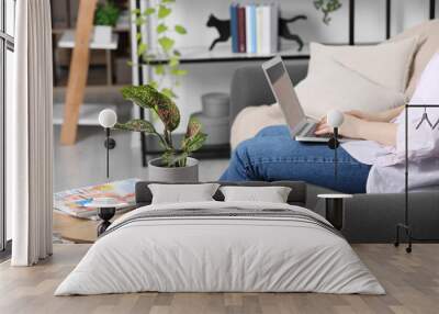 Woman using laptop in living room, focus on houseplant Wall mural