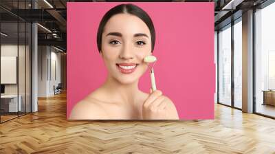 Woman using natural jade face roller on pink background, space for text Wall mural