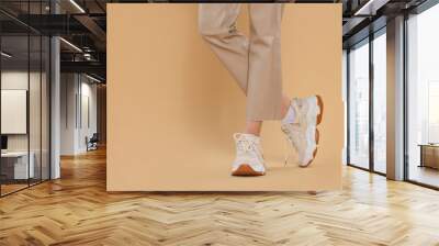 Woman wearing pair of new stylish sneakers on beige background, closeup. Space for text Wall mural