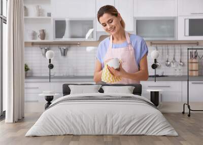 Woman wiping ceramic cup at table with clean dishes in kitchen Wall mural