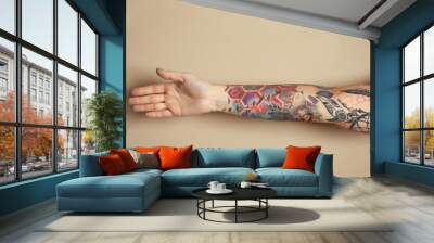 Woman with colorful tattoos on arm against beige background, closeup Wall mural