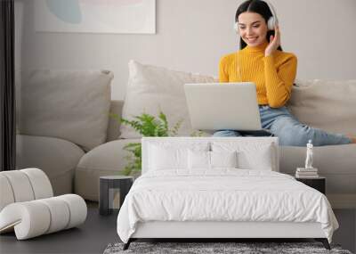 Woman with laptop and headphones sitting on sofa at home Wall mural