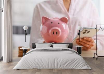 Woman with piggy bank and smartphone at table indoors, closeup Wall mural