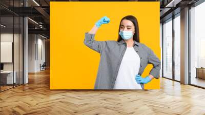 Woman with protective mask and gloves showing muscles on yellow background, space for text. Strong immunity concept Wall mural