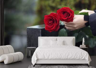 Woman with red roses near black granite tombstone outdoors, closeup. Funeral ceremony Wall mural