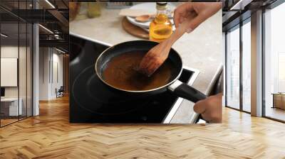 Woman with wooden spatula and frying pan of used cooking oil near stove, closeup Wall mural