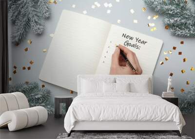 Woman writing in notebook at light grey table with Christmas decor, top view. New Year aims Wall mural