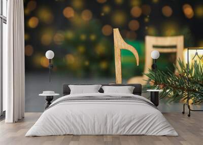 Wooden music note and fir branches on light grey table against blurred Christmas lights Wall mural