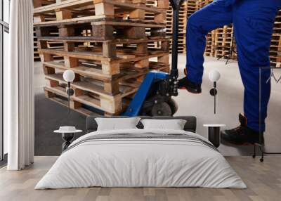 Worker moving wooden pallets with manual forklift in warehouse, closeup Wall mural