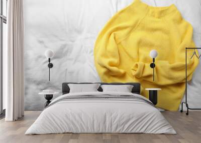 Yellow warm sweater on white bedsheet, top view. Space for text Wall mural