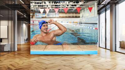 Young athletic man wearing cap and goggles in swimming pool Wall mural