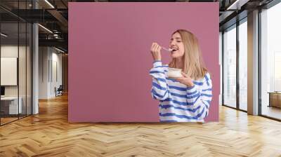 Young attractive woman eating tasty yogurt on color background Wall mural