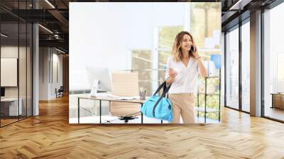 Young beautiful businesswoman holding fitness bag in office. Space for text Wall mural