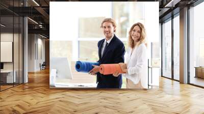 Young businessman and businesswoman holding yoga mats in office. Gym after work Wall mural