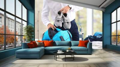 Young businessman packing sports stuff for training into bag in office Wall mural