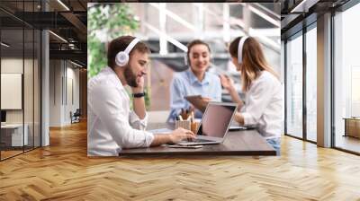 Young businessman with headphones, laptop and his colleagues at table in office Wall mural