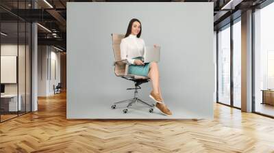 Young businesswoman with laptop sitting in comfortable office chair on grey background Wall mural