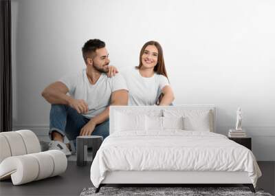 Young couple in stylish jeans sitting near white wall Wall mural