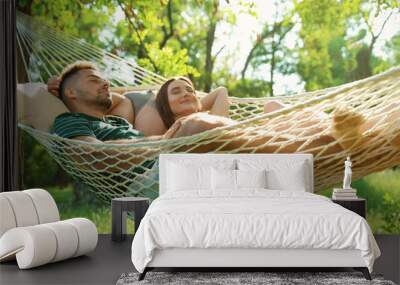 Young couple resting in comfortable hammock at green garden Wall mural