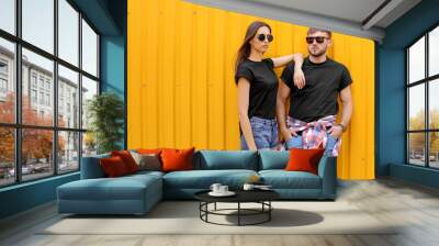 Young couple wearing black t-shirts near color wall on street Wall mural