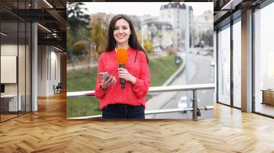 Young female journalist with microphone and smartphone working on city street. Space for text Wall mural