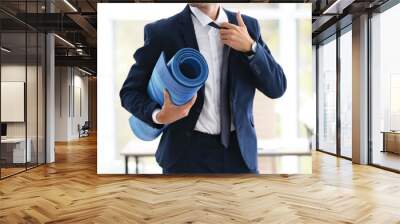 Young handsome businessman holding yoga mat in office. Gym after work Wall mural