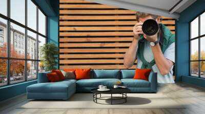 Young male photographer with professional camera near wooden wall. Space for text Wall mural