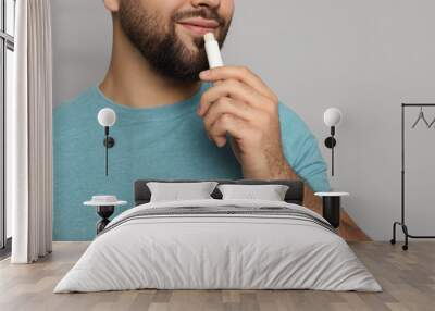 Young man applying lip balm on grey background, closeup Wall mural