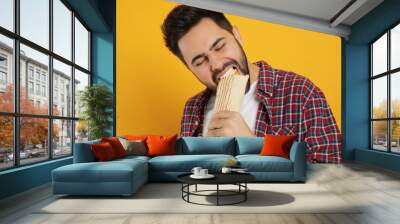 Young man eating tasty shawarma on yellow background Wall mural