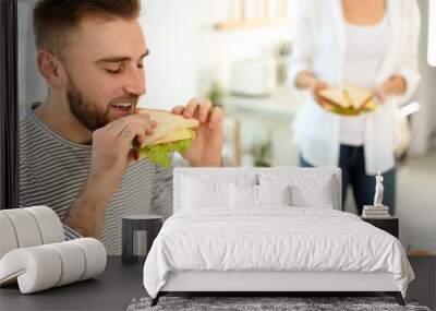 Young man having breakfast with sandwiches in kitchen, space for text Wall mural