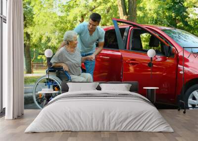 Young man helping disabled senior woman in wheelchair to get into car outdoors Wall mural