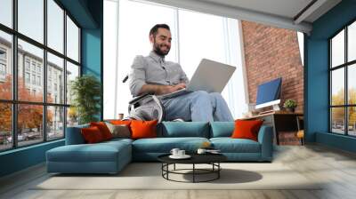 Young man in wheelchair using laptop at office Wall mural