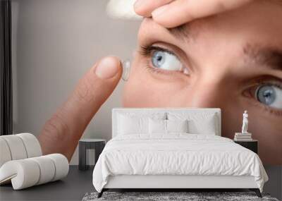 Young man putting contact lens in his eye on light background Wall mural