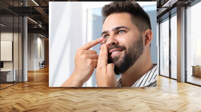 Young man putting in contact lens indoors Wall mural