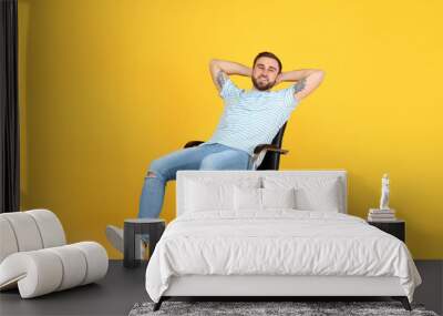 Young man relaxing in comfortable office chair on yellow background Wall mural