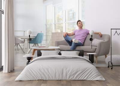 Young man relaxing on sofa under air conditioner at home Wall mural