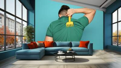 Young man scratching back with toy rake on color background. Annoying itch Wall mural