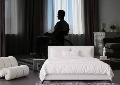 Young man sitting in wheelchair near window indoors Wall mural