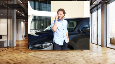 Young man talking on phone near modern car, outdoors Wall mural