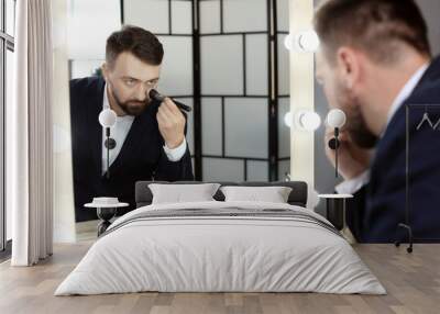 Young man using makeup brush near mirror in dressing room Wall mural