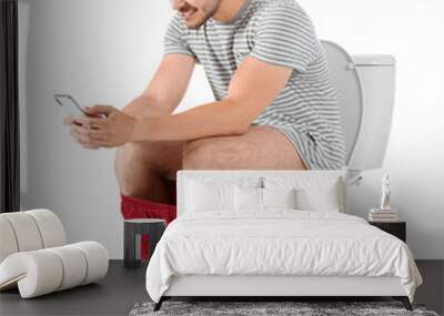 Young man using mobile phone while sitting on toilet bowl. Isolated on white Wall mural