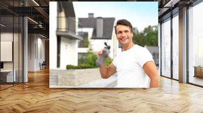 Young man with earphones drinking water after running on street. Healthy lifestyle Wall mural