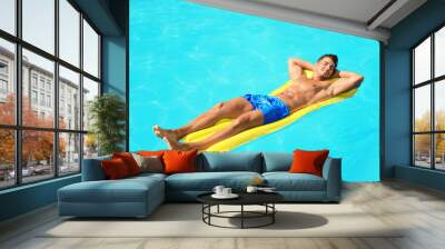 Young man with inflatable mattress in pool on sunny day Wall mural