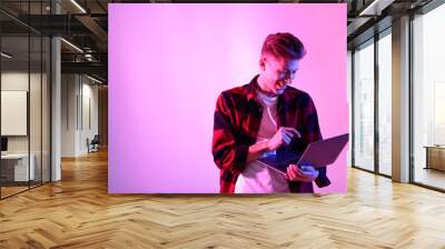 Young man with laptop talking via video chat on pink background in neon lights. Space for text Wall mural