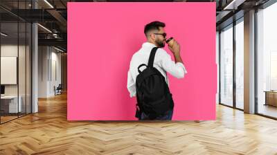 Young man with stylish backpack and cup of coffee on pink background. Space for text Wall mural