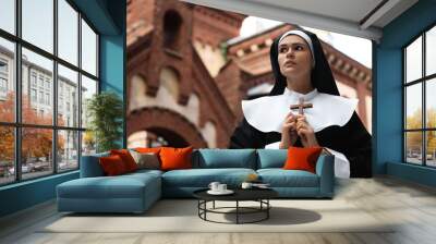 Young nun holding Christian cross near building outdoors, space for text Wall mural