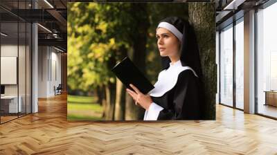 Young nun reading Bible in park on sunny day Wall mural